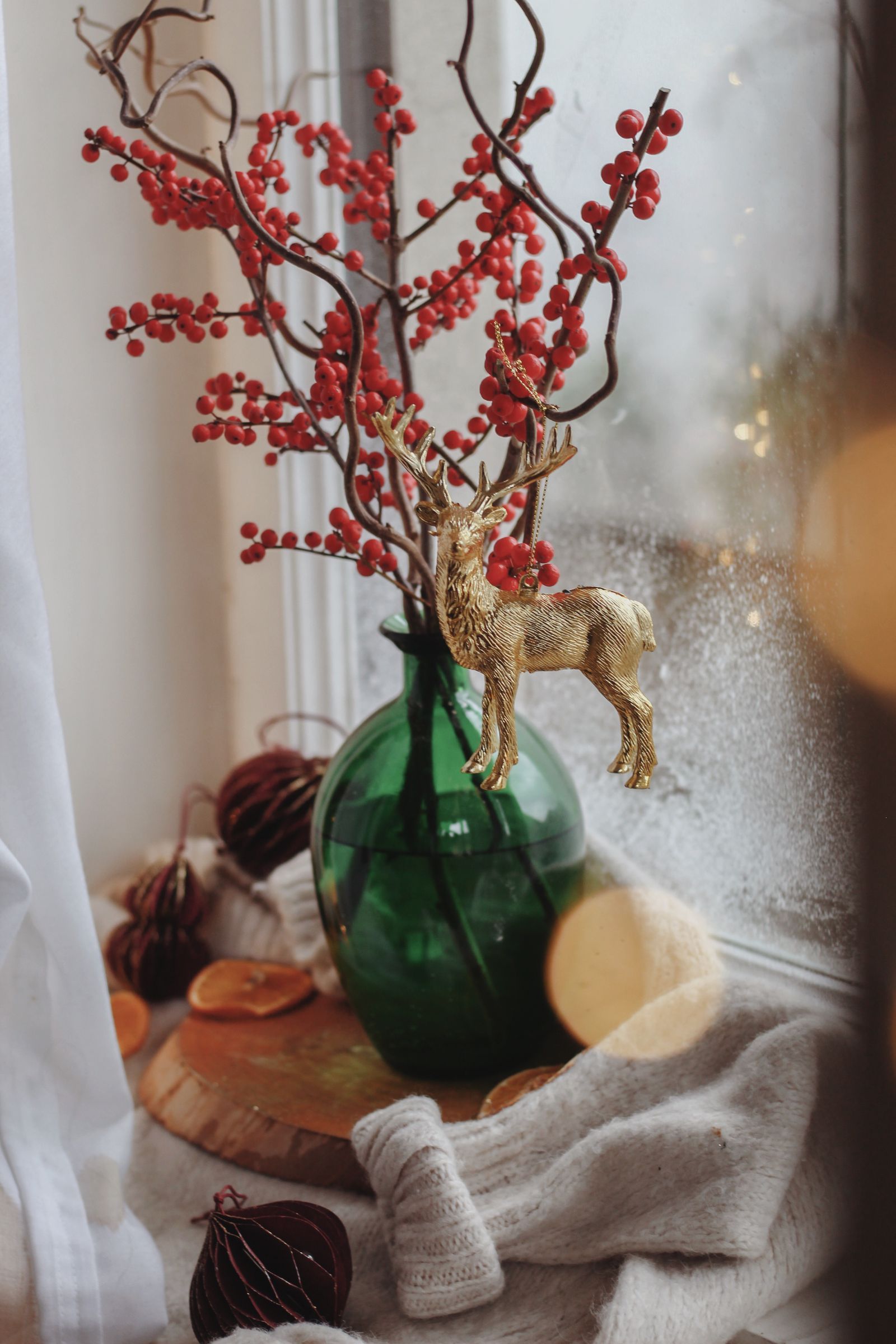 Red winter berries in a green glass vase with a gilded deer on a frosted windowsill