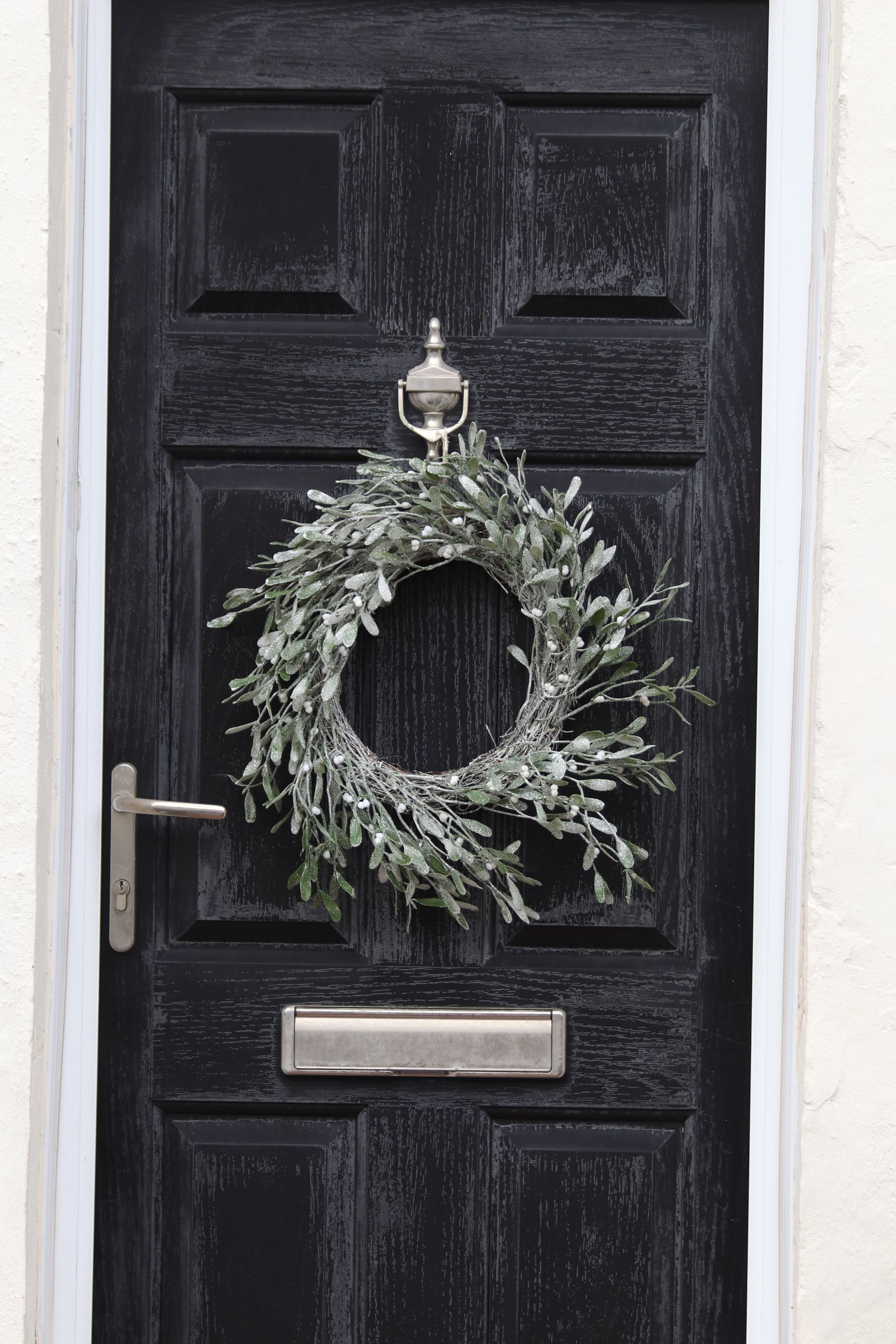 A silvery olive-leaf wreath on a black panelled front door