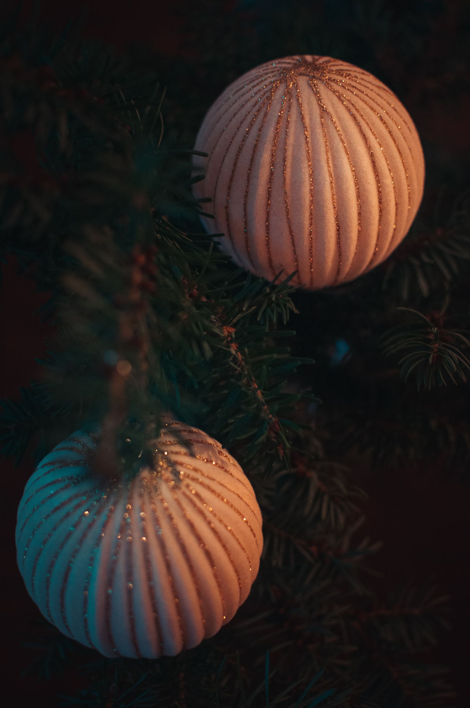 Two hand-painted ribbed baubles hanging in a dark Christmas tree