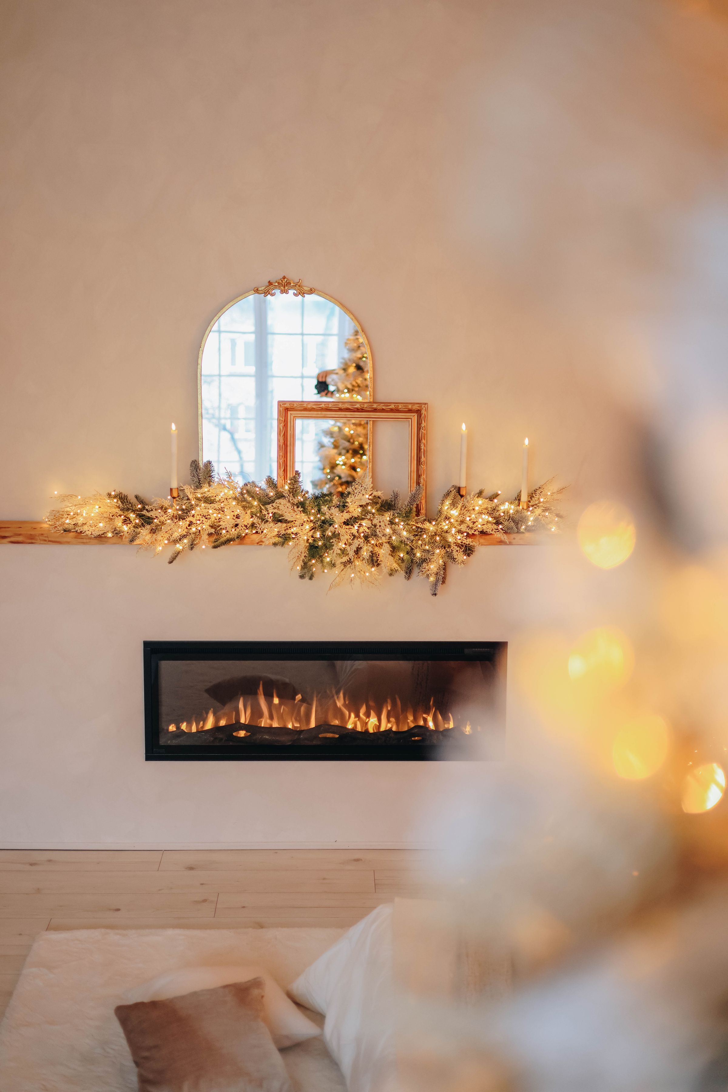 A softly glowing mantelpiece garland beneath an arched gilt mirror, seen through tree lights