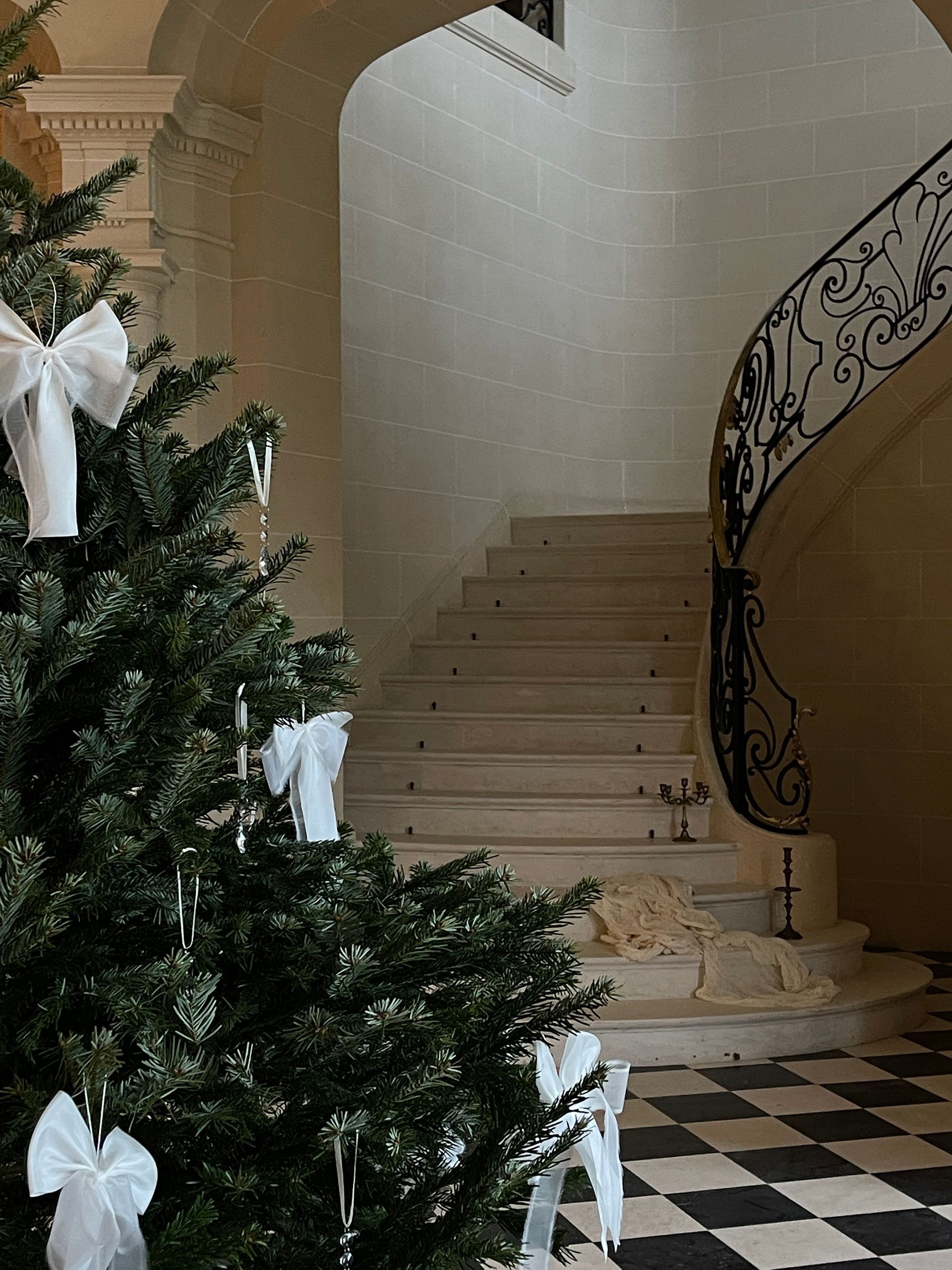 A tree tied with white bows beside a sweeping stone staircase and chequered floor