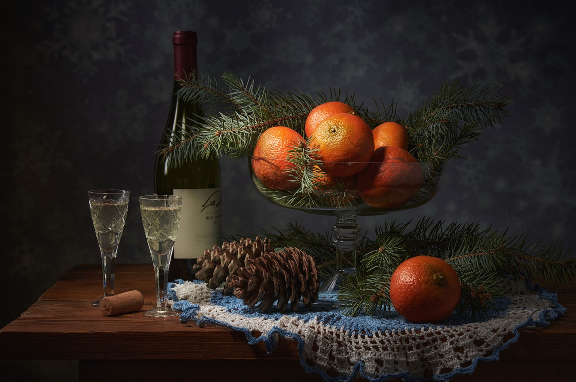 A painterly still life of tangerines, pine, pinecones and wine on a lace cloth