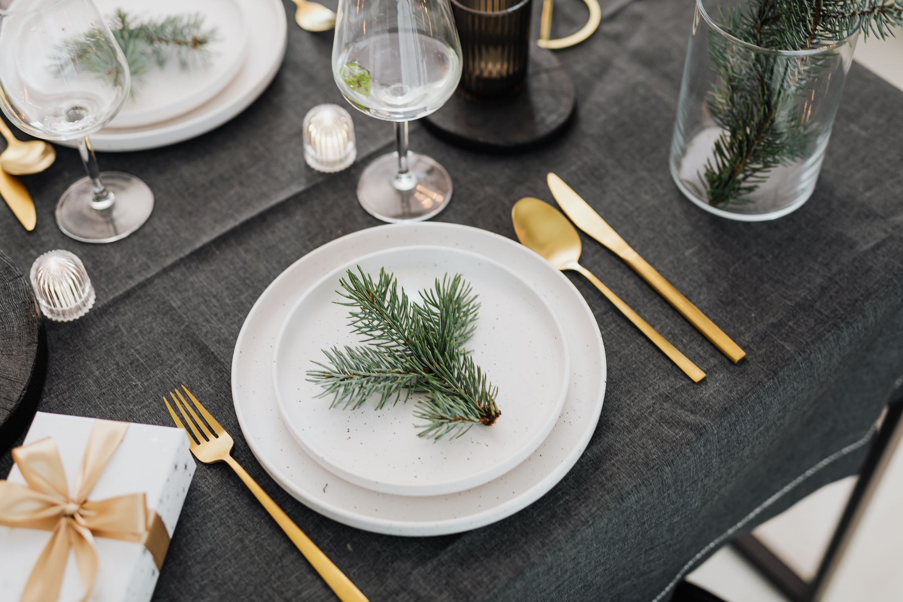 A charcoal-linen table set with a pine sprig on white china and brushed-gold cutlery