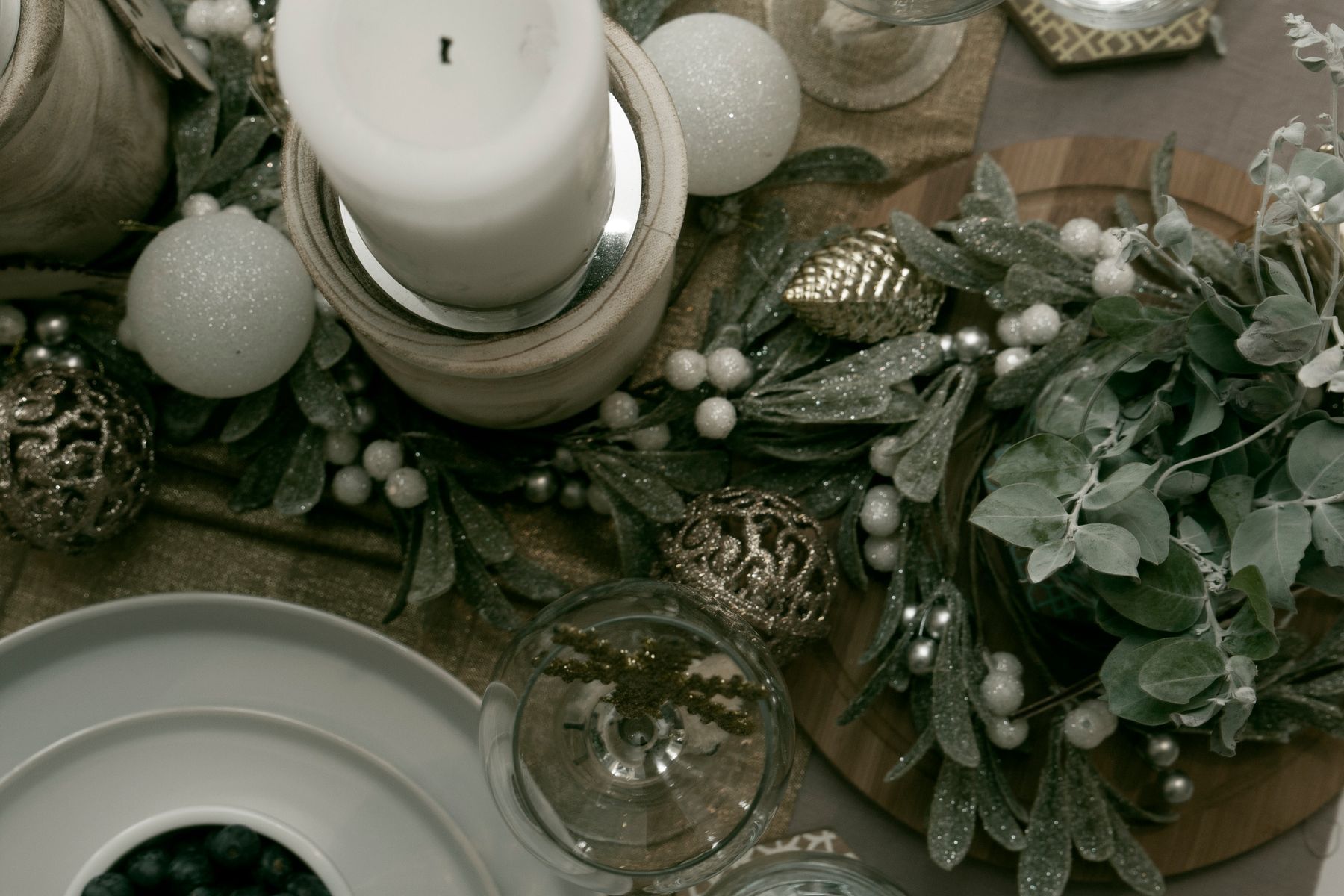 A table styled with silvery foliage, white berries, a pillar candle and pale baubles