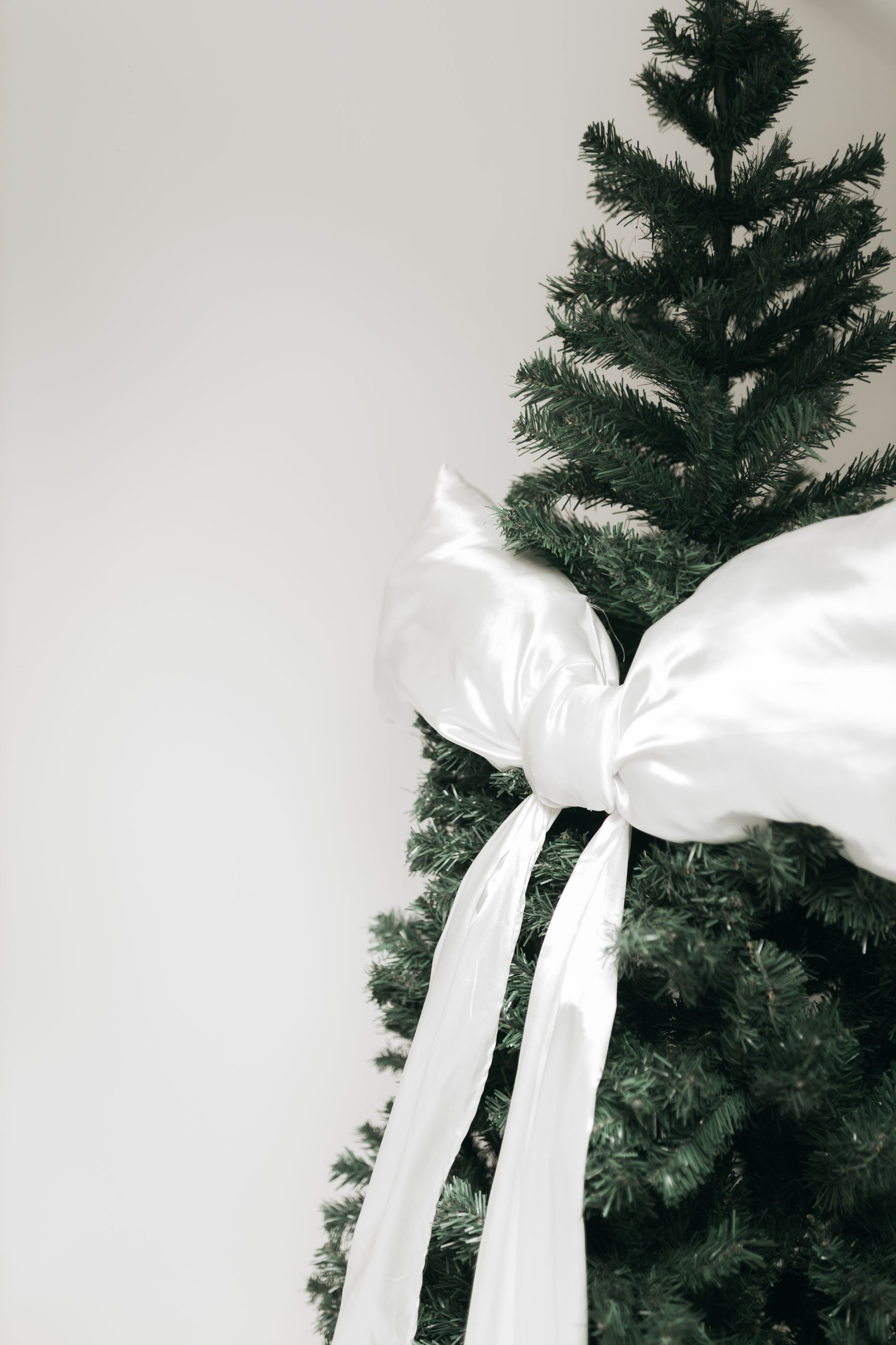 A single oversized ivory satin bow tied onto a Christmas tree